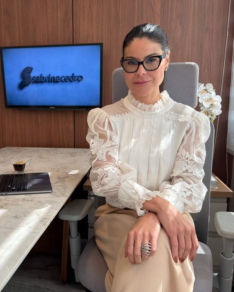 Sabrina Cedro sentada no consultório, com o logo da marca na tela ao fundo